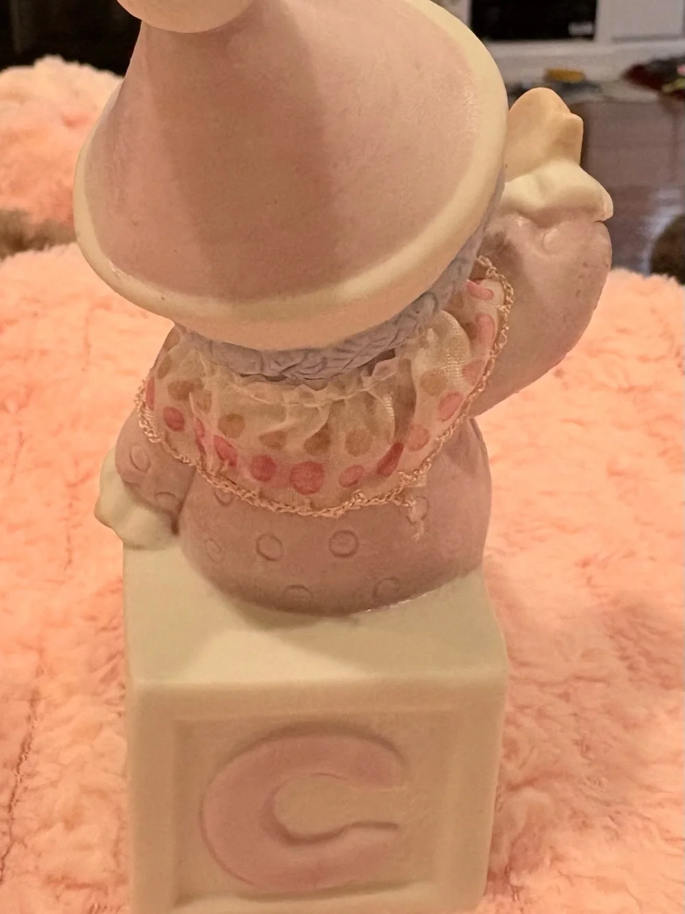 Hand -painted pastel pink-clad baby clown wearing a textured hat.